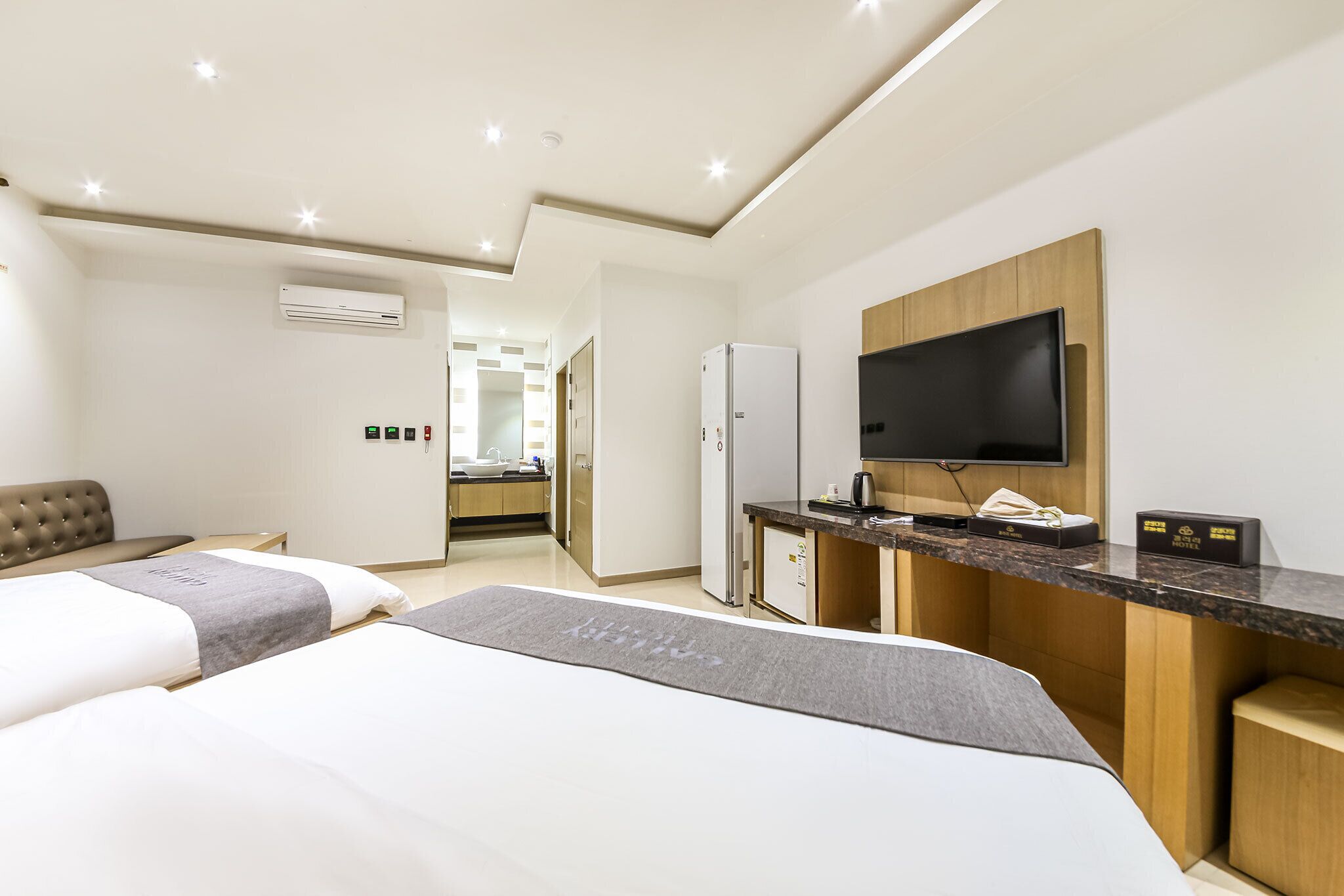 A hotel room with two beds, a kitchenette, a TV, and a minibar.