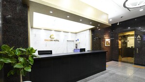 A reception desk with a marble wall and a potted plant. - Gallery Hotel (Gwangju)