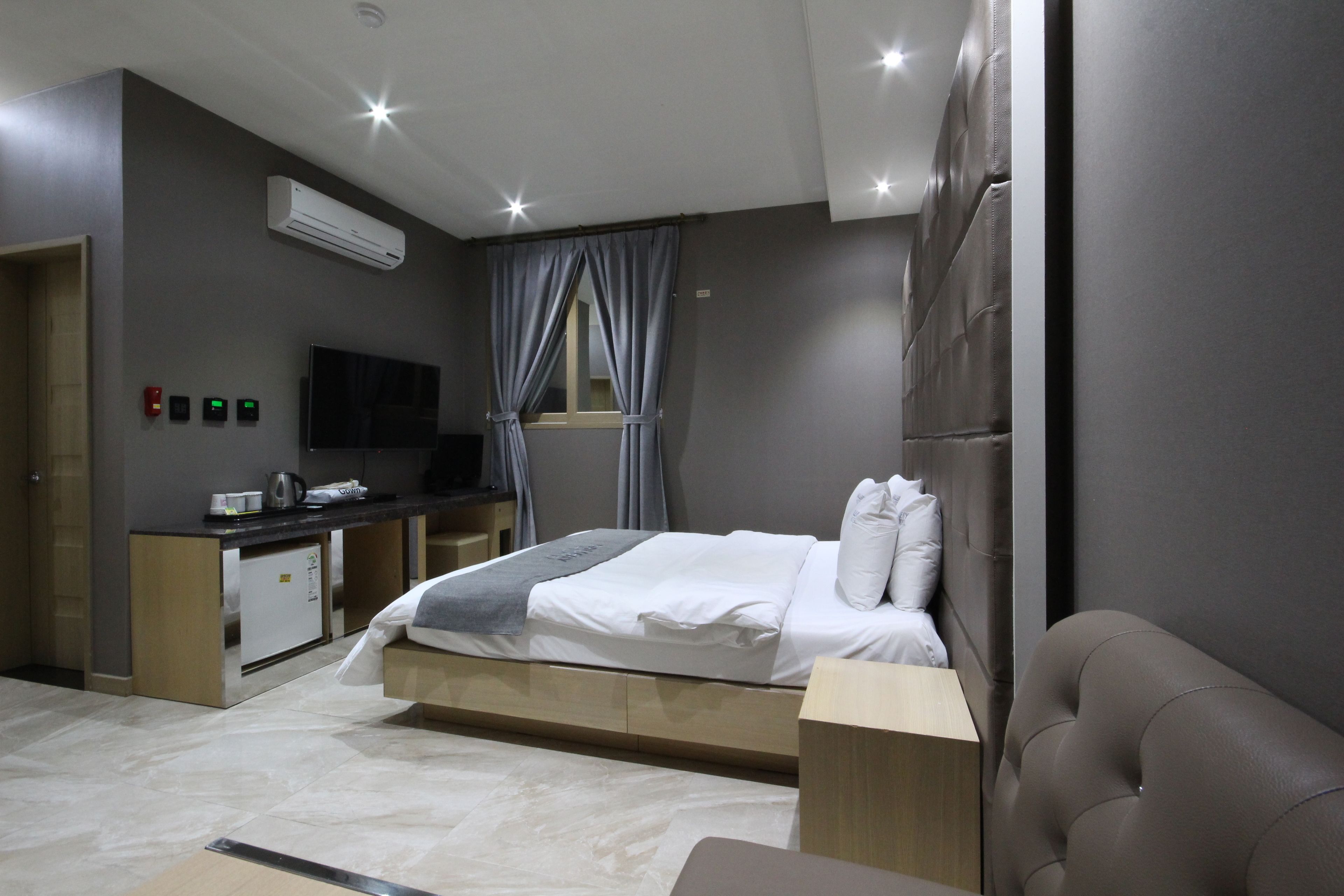 Une chambre d’hôtel moderne équipée d’un lit, d’un bureau, d’une télévision à écran plat, d’un climatiseur et d’une petite kitchenette.