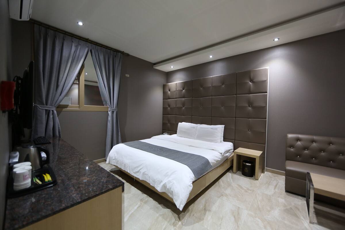 Una habitación de hotel moderna con una cama grande, una mesita de noche, un escritorio pequeño y un área de descanso.