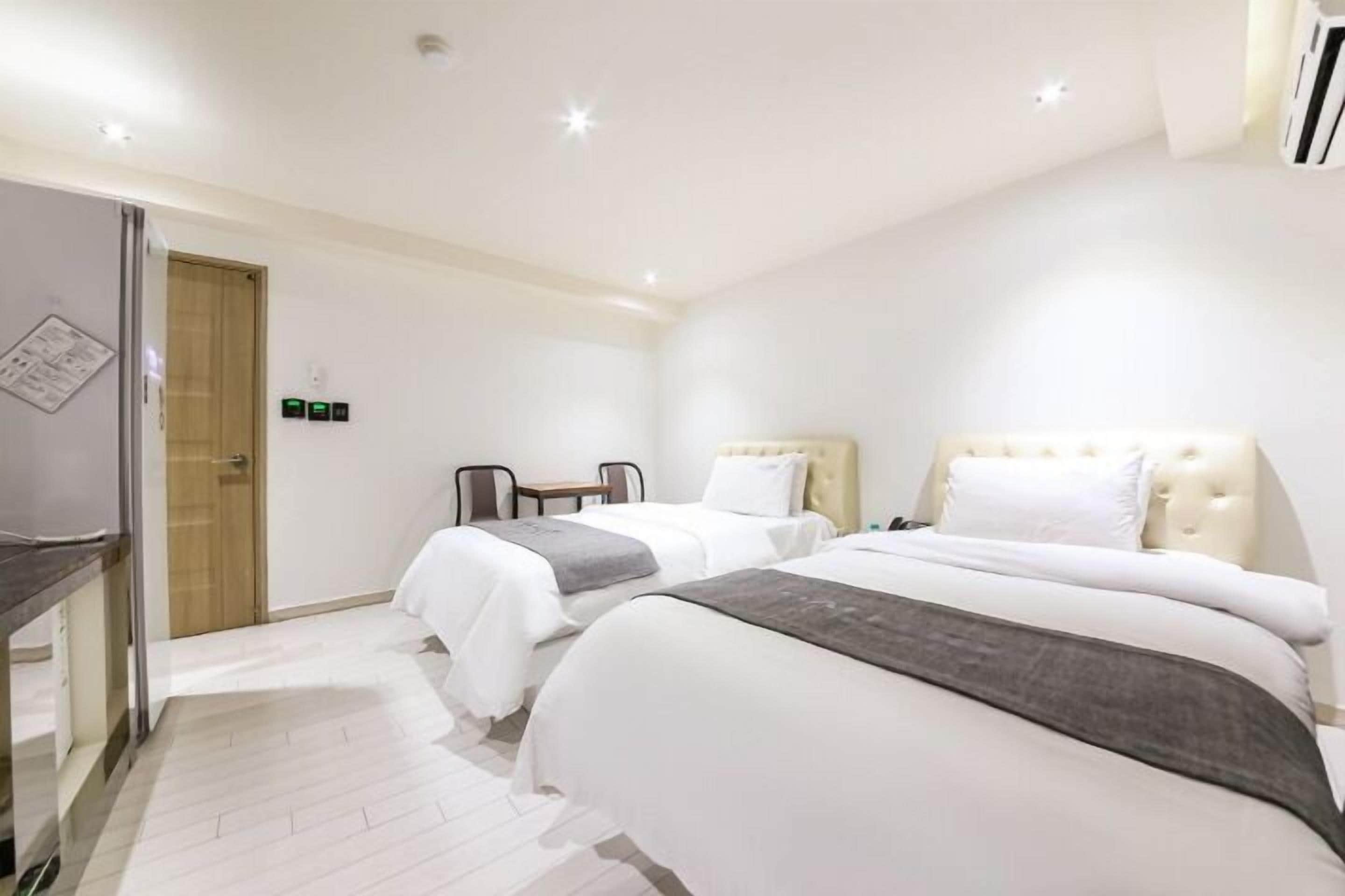 A hotel room with two beds, a desk, and a chair. There is a door and an air conditioning unit on the wall.