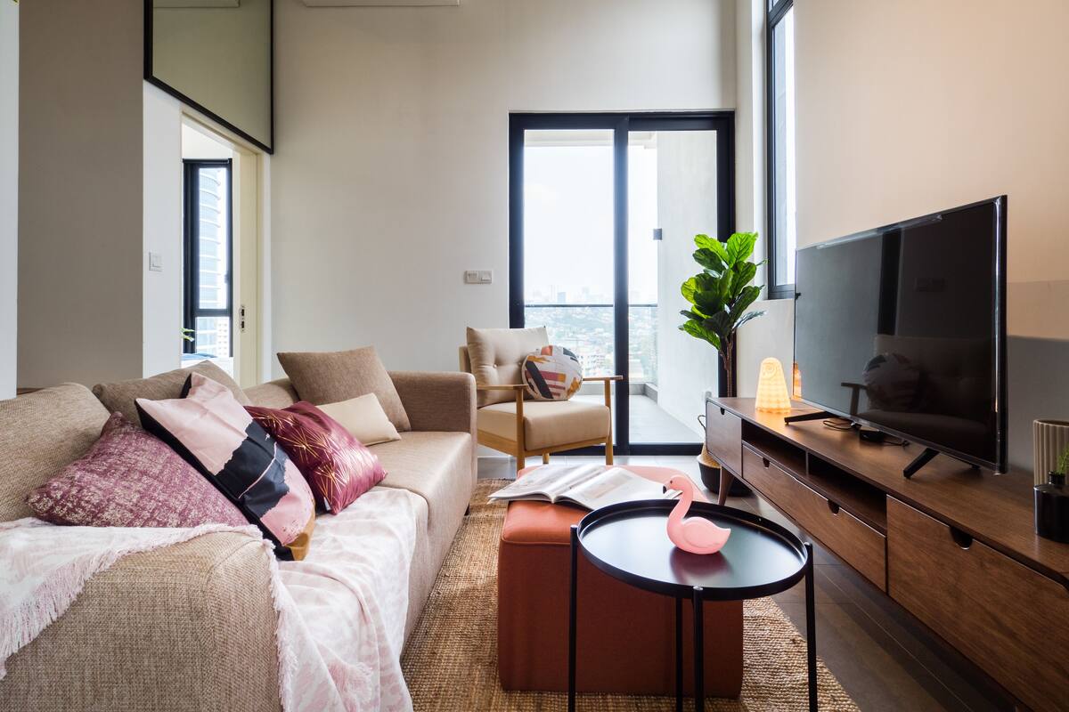 A modern living room with a sofa, armchair, and ottoman, a television, and a view through a large window.
