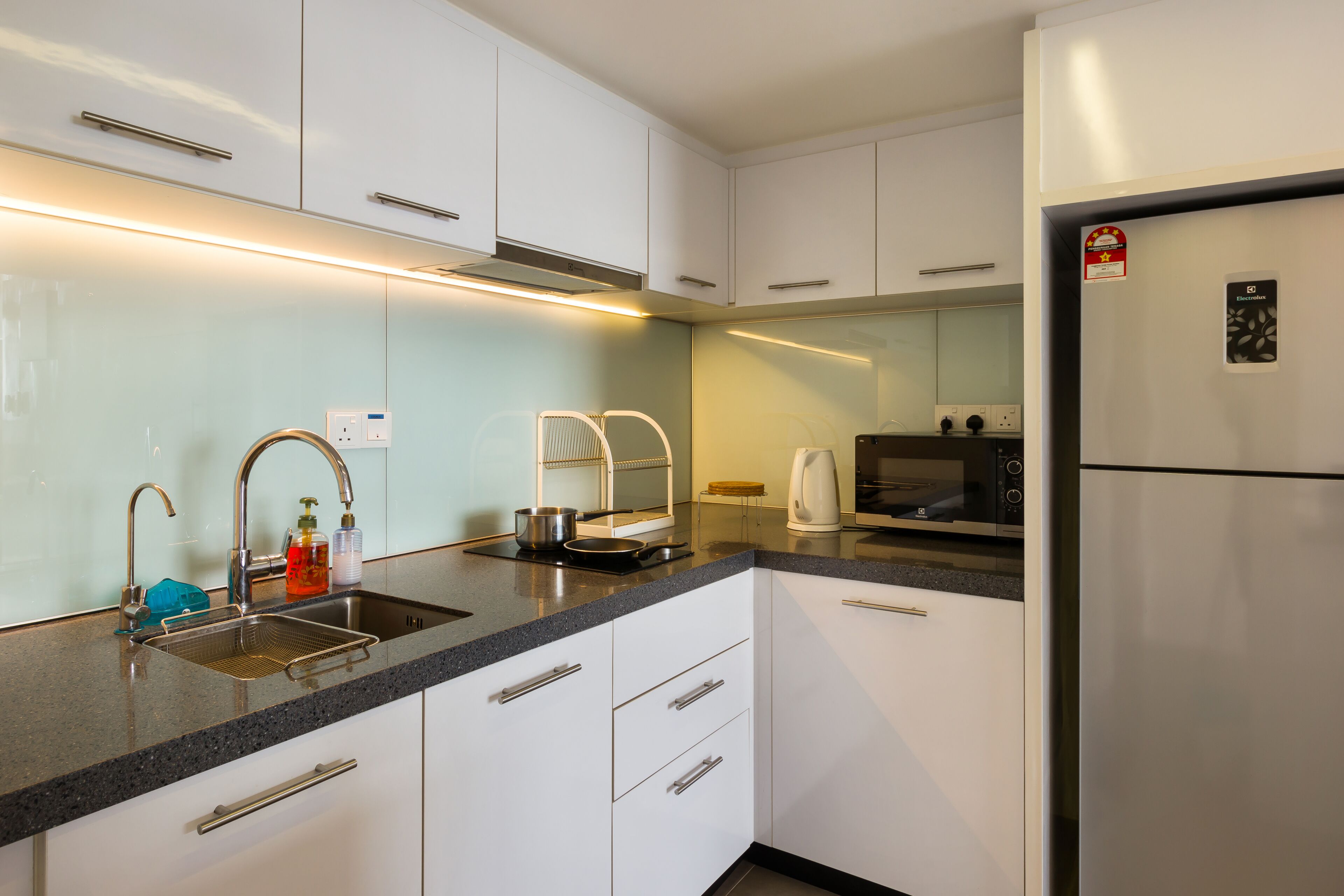 A modern kitchen with white cabinets, a stainless steel refrigerator, a microwave, and a kettle.