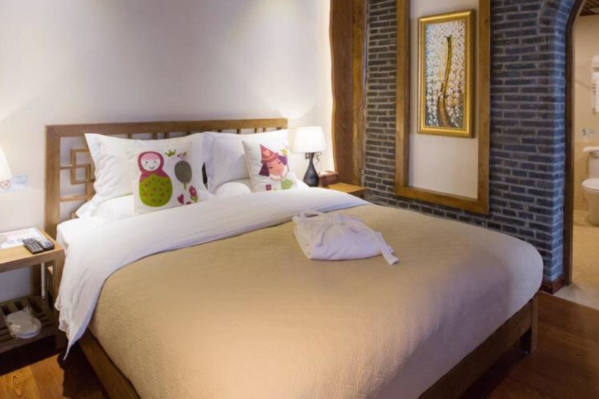 Une chambre d’hôtel avec un plafond en bois, un mur en briques et un lit recouvert de draps blancs et agrémenté d’oreillers colorés.