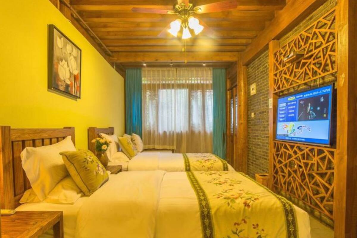 Une chambre d’hôtel avec deux lits, des têtes de lit en bois, un ventilateur de plafond, un téléviseur fixé au mur et un panneau décoratif mural.