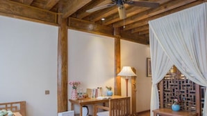 Une pièce chaleureuse avec des poutres apparentes, un ventilateur de plafond, une table à manger avec des chaises, une table d’appoint avec une lampe et un paravent décoratif.