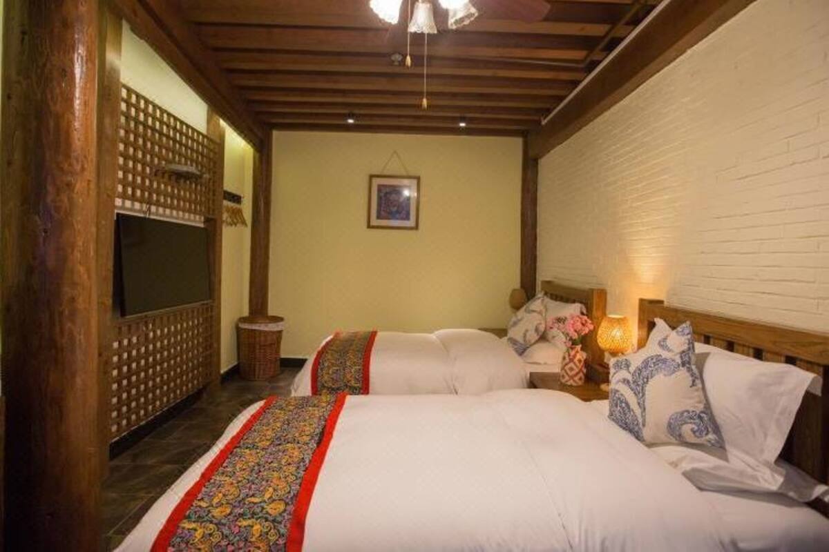Une chambre avec deux lits, des poutres en bois au plafond, un téléviseur fixé au mur et une petite table ronde avec une lampe.