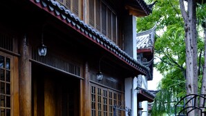Une cour traditionnelle avec un bâtiment en bois, un chemin de pierre et un espace extérieur aménagé avec des chaises et des tables.