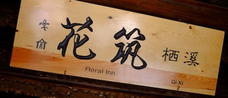 A wooden sign with Chinese characters and the words "Floral Inn" and "Qi Xi" indicating the name of the establishment.