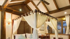 Une chambre à coucher avec un lit à baldaquin, des poutres apparentes, un ventilateur de plafond et une fenêtre avec des rideaux.