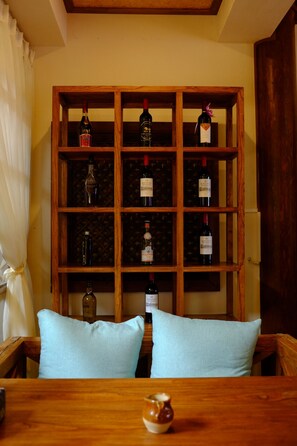 Un porte-bouteilles en bois contenant plusieurs bouteilles, une table avec une carafe et deux coussins bleu clair.