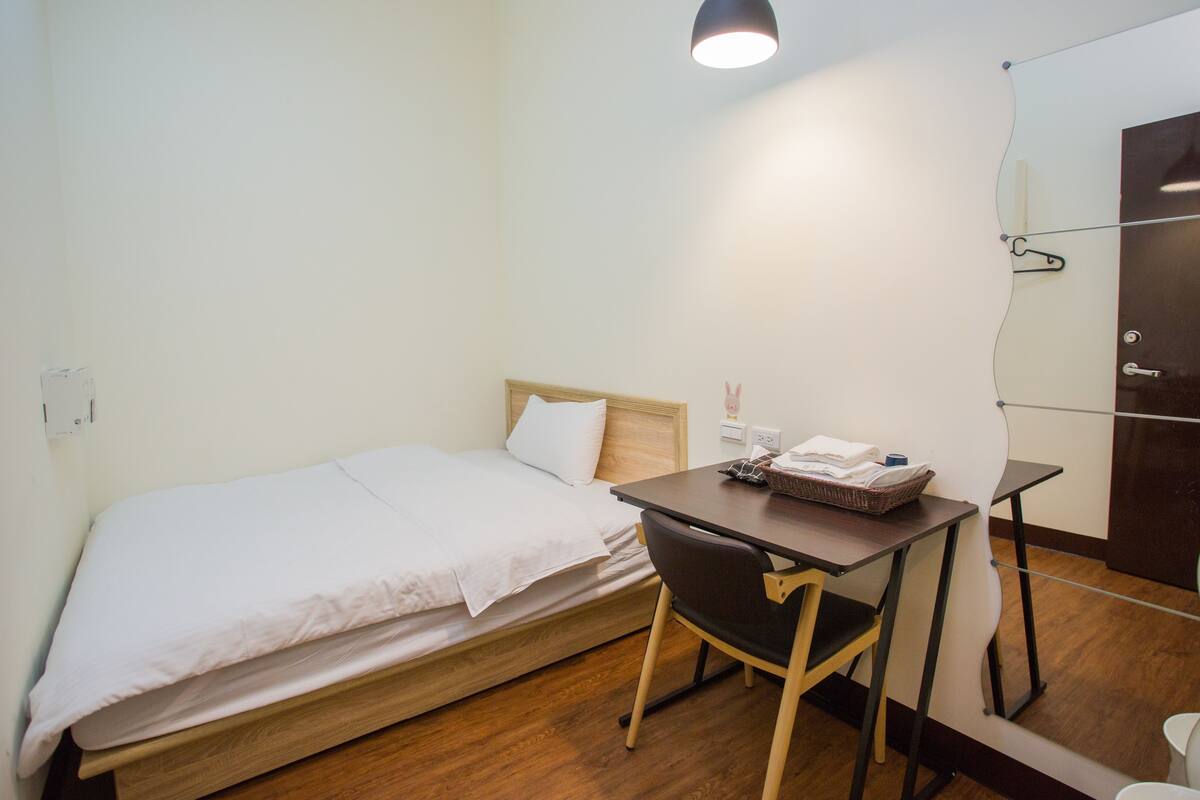 Ein kleines Zimmer mit einem Einzelbett, einem Schreibtisch und einem Stuhl.