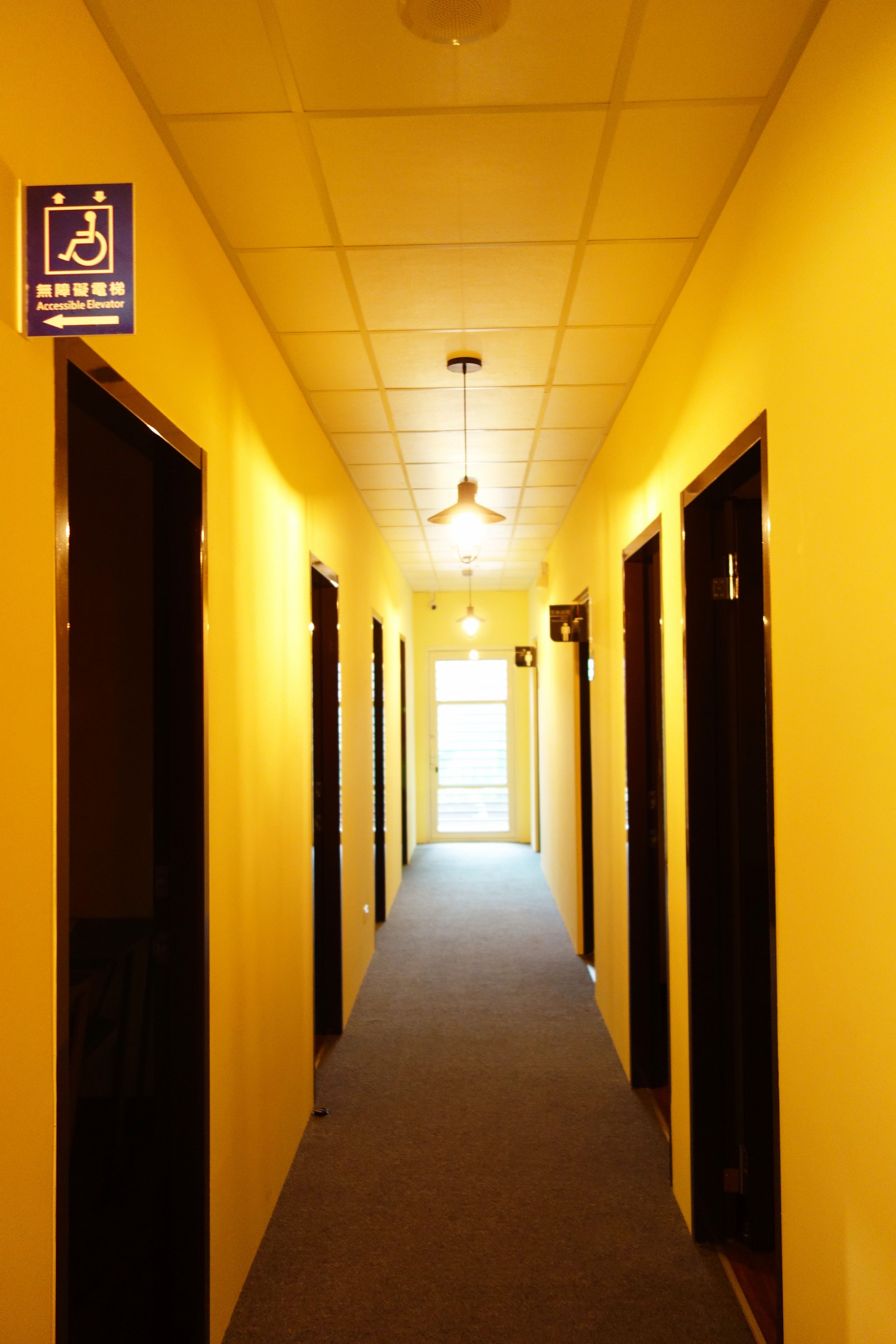 A corridor with yellow walls, a ceiling fan, and doors on both sides.