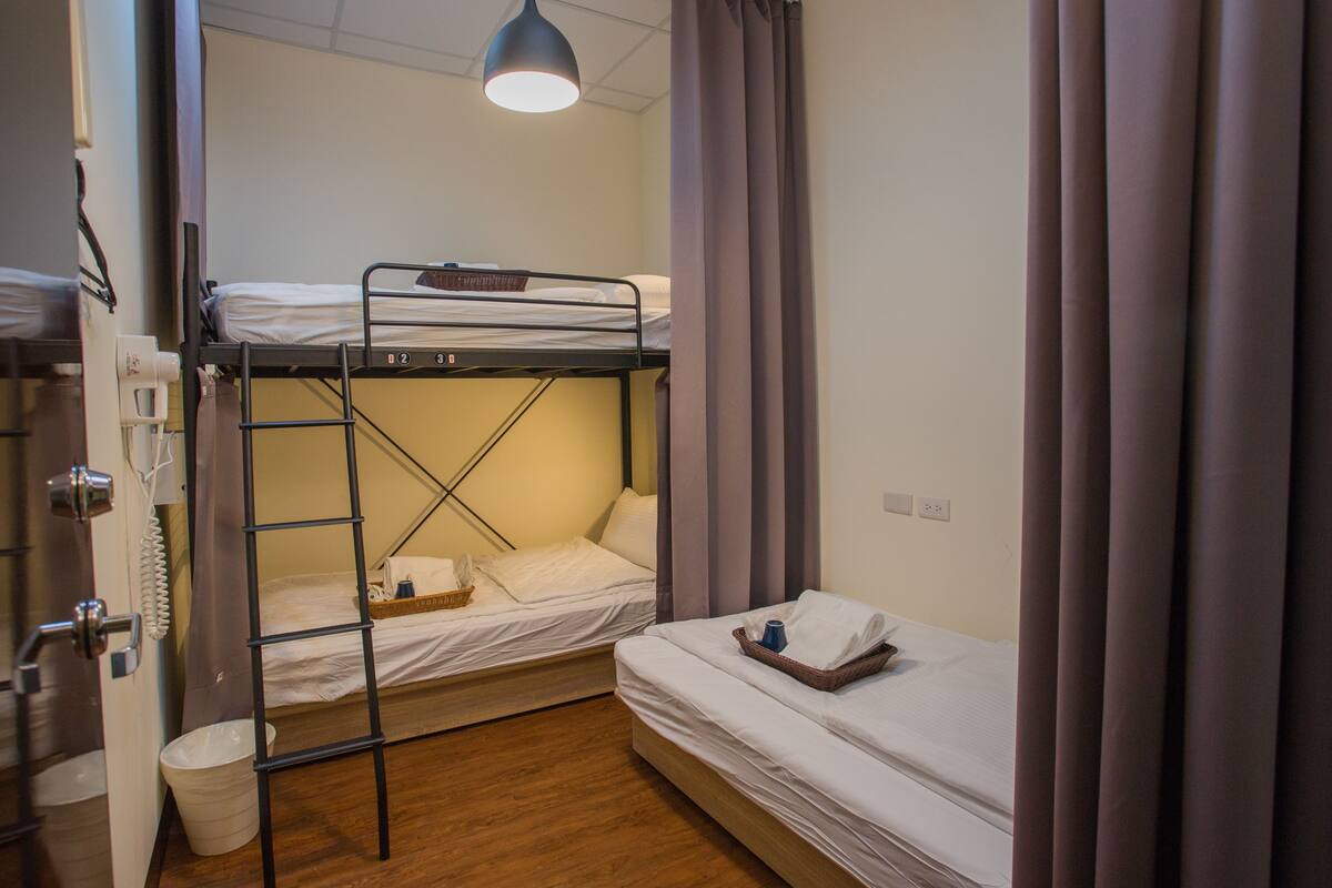 Ein Schlafsaalzimmer mit Stockbetten, einem Schreibtisch, einem Stuhl, einer Lampe und einem Fenster mit Vorhängen.