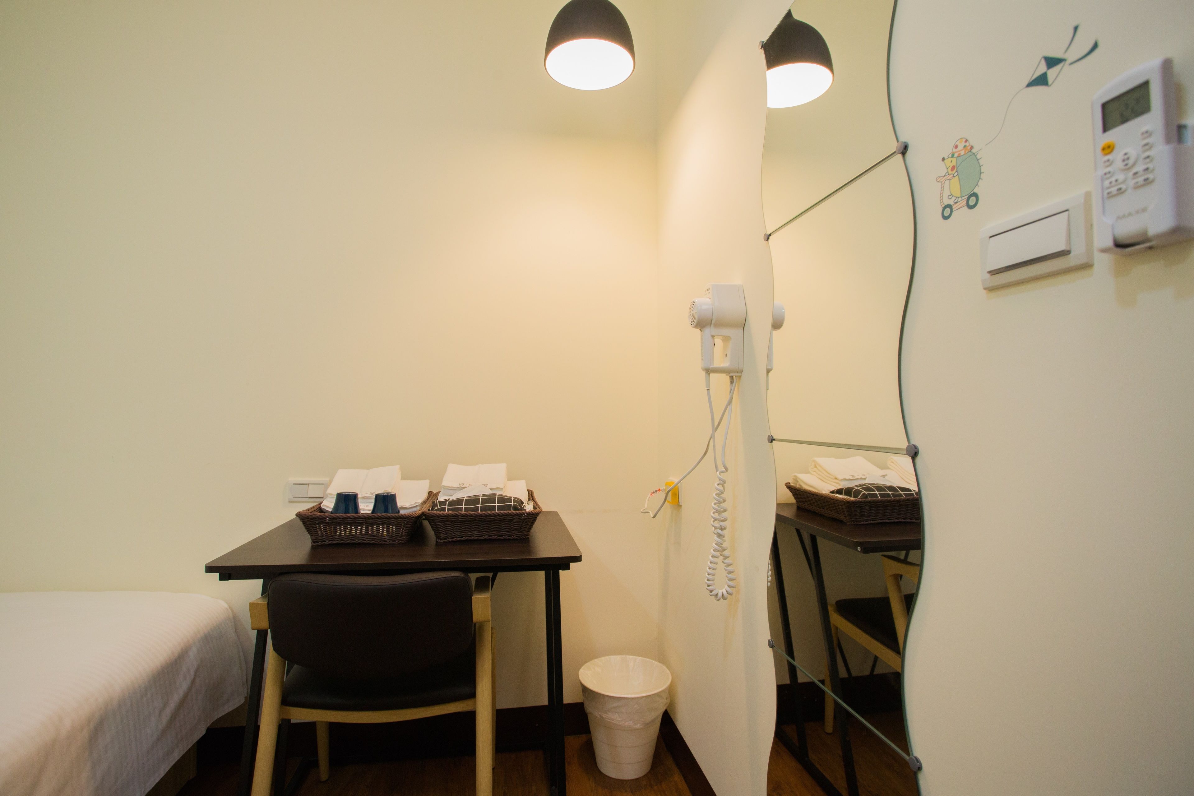 A small, compact room with a single bed, a desk with a chair, a telephone, and a waste bin.