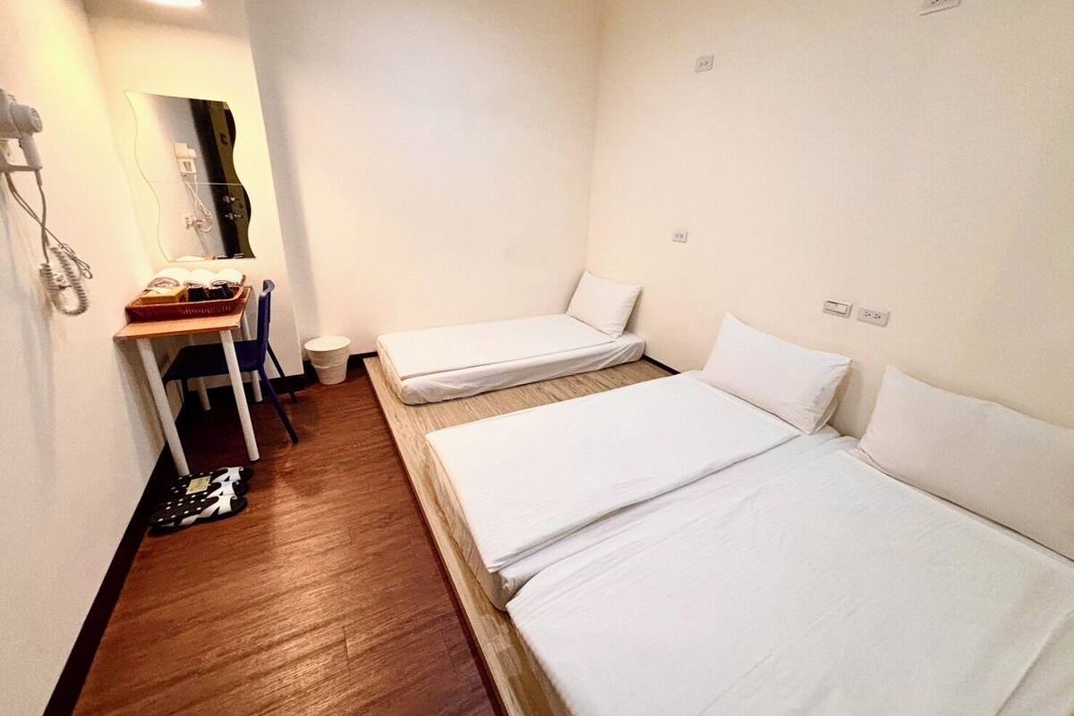 Ein kleines, sauberes Zimmer mit zwei Einzelbetten, einem Schreibtisch mit Stuhl, einem Spiegel und einer kleinen Mülltonne.