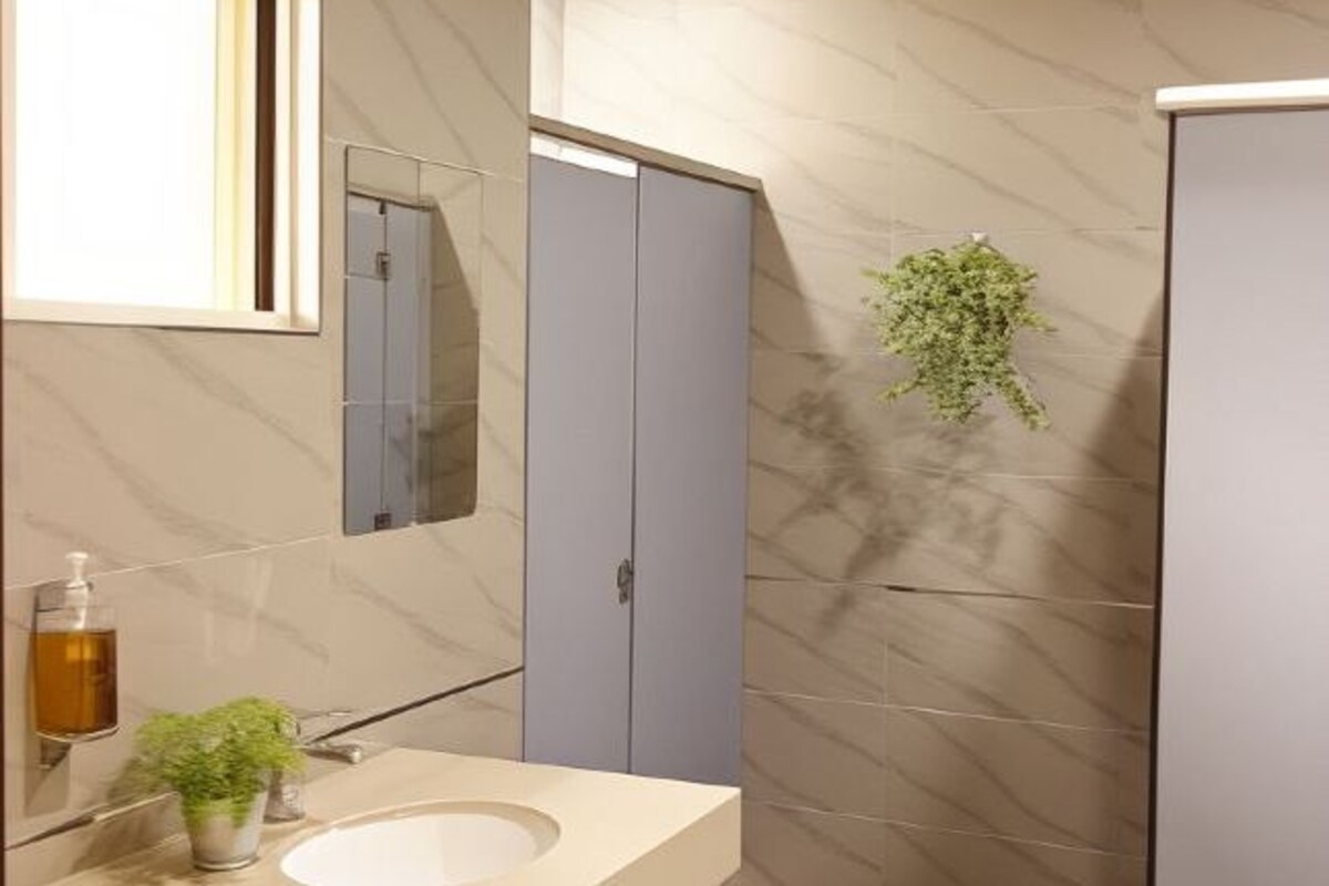 A modern bathroom with a marble-tiled wall, a sink with a mirror, a plant, and a cabinet.