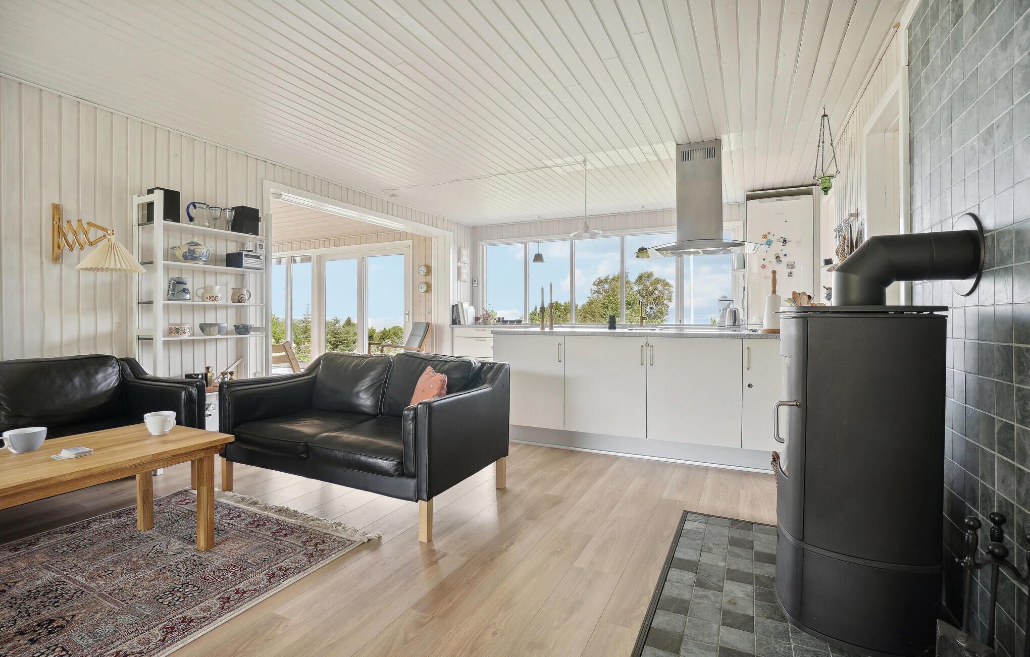 A modern kitchen with white cabinets, a black stove, and a view of the outdoors through large windows.