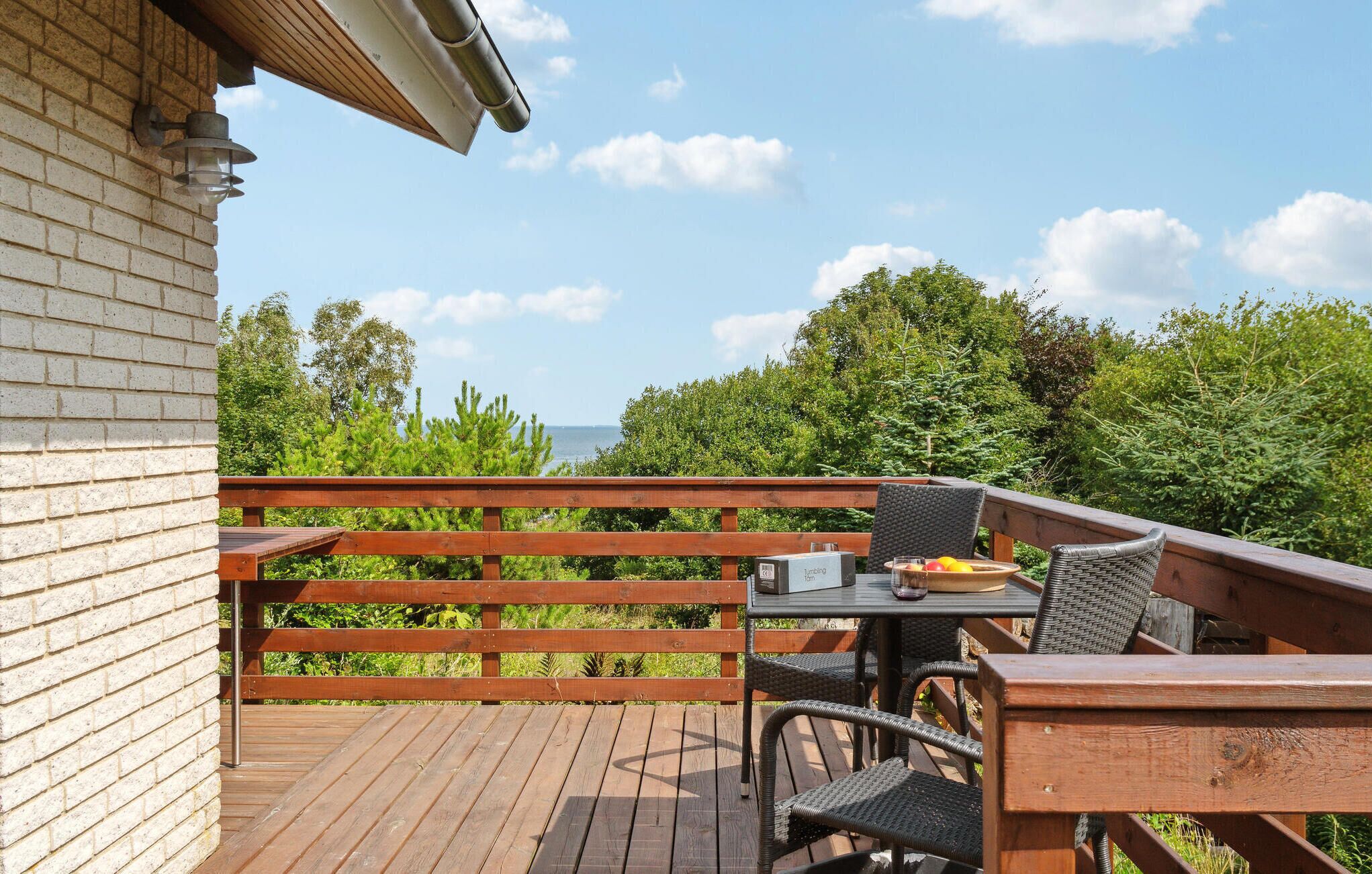 Une terrasse en bois avec une table et des chaises, donnant sur une étendue d’eau et une zone verdoyante.