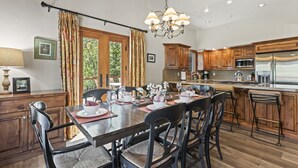A modern kitchen with wooden cabinets, a stainless steel refrigerator, and a dining area with a table set for four. - Rare 3BR + Den 2-Min Walk to Park City Ski Base! (Park City)