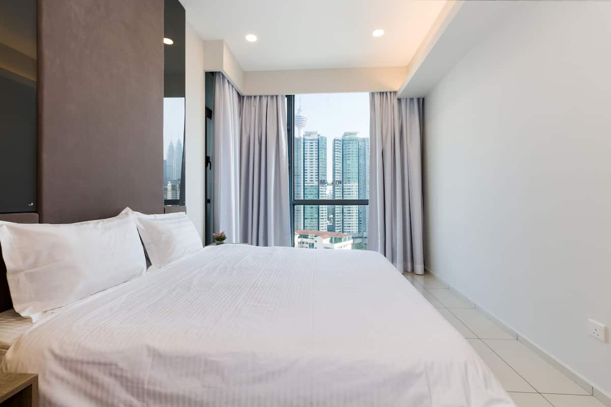 Une chambre d’hôtel avec un grand lit, une vue sur de hauts immeubles et une fenêtre avec des rideaux.
