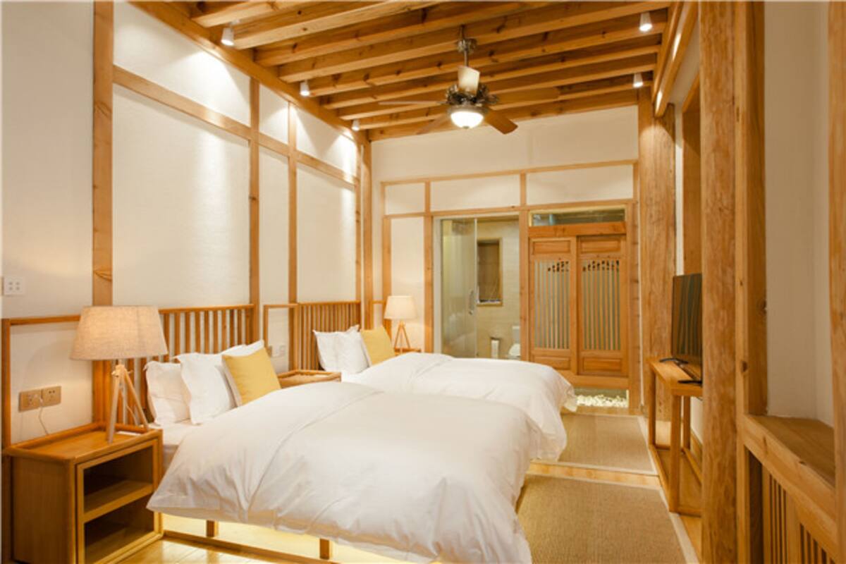 Habitación de hotel con dos camas, cabeceros de madera, ventilador de techo y un espejo grande.