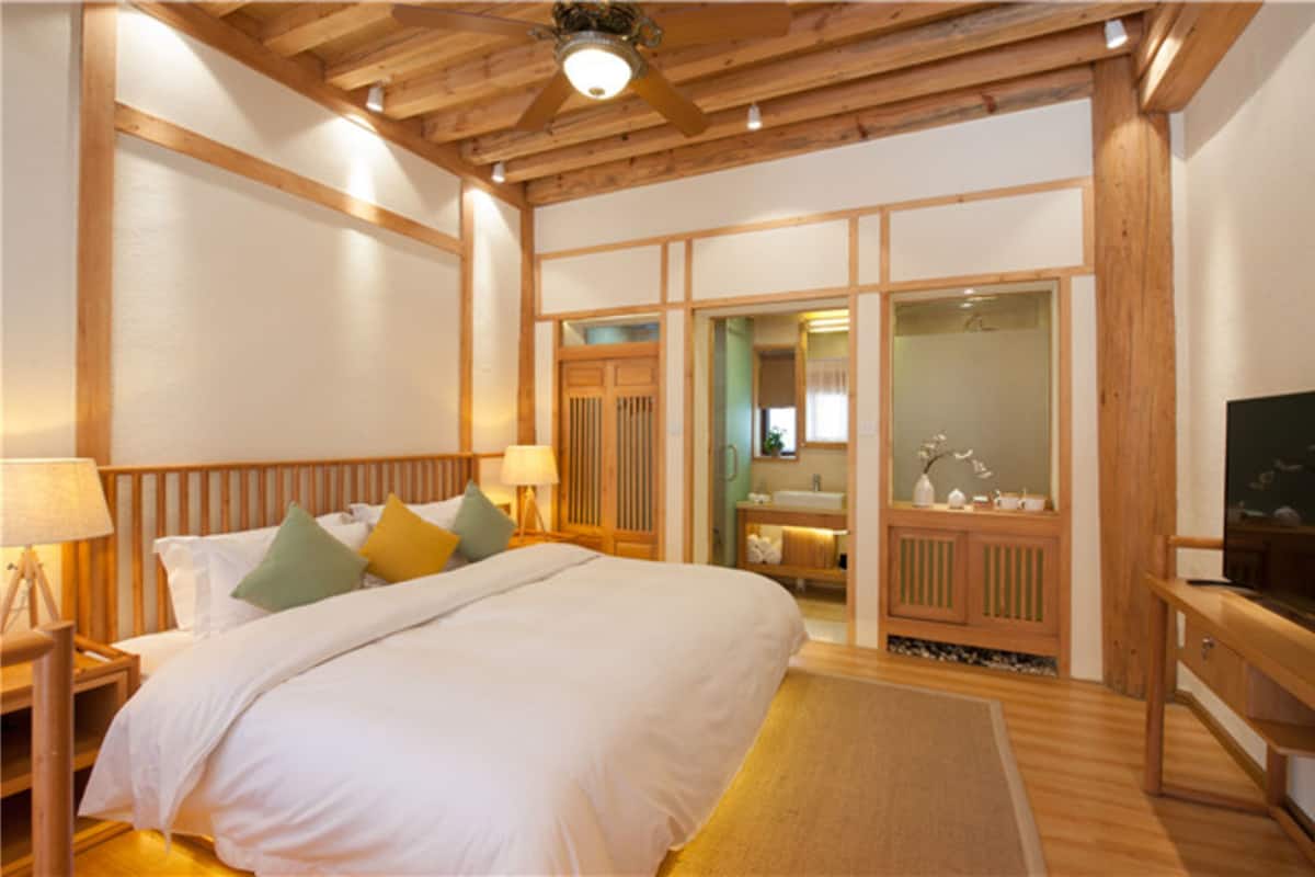 Un dormitorio con una cama grande, cabecera de madera, mesitas de noche con lámparas, un televisor y una puerta corredera que da al baño.