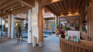 Interior de madera con mostrador de recepción, plantas en macetas y vistas al área exterior.