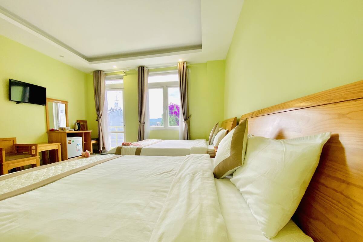 A hotel room with two beds, a desk, a television, and a window with curtains.