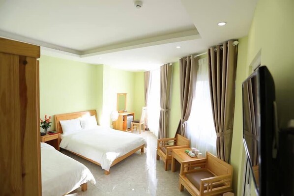 A hotel room with two single beds, a wooden desk, a chair, a TV, and a window with curtains.