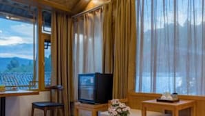 A cozy room with a wooden ceiling, a large window with curtains, a television, a small table with a vase of flowers, and a sofa. - Floral Hotel Lijiang Banshanyunfu (Lijiang)