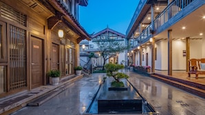 Un patio tradicional con edificios de madera, una fuente central y plantas en macetas.