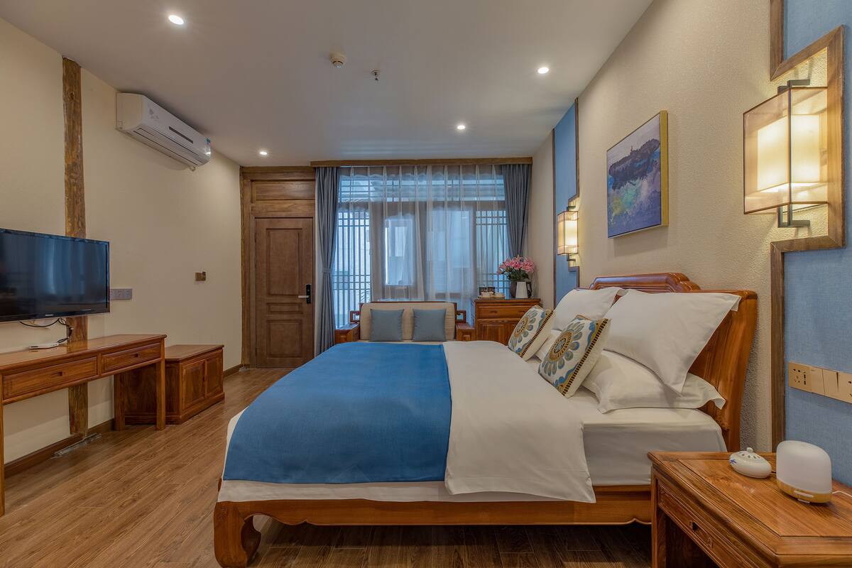 Een hotelkamer met een houten bed, een televisie, een bureau en een raam met gordijnen.