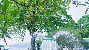 A swimming pool with a dolphin statue, surrounded by trees and a water slide. - Mutiara Carita Cottages (Carita)