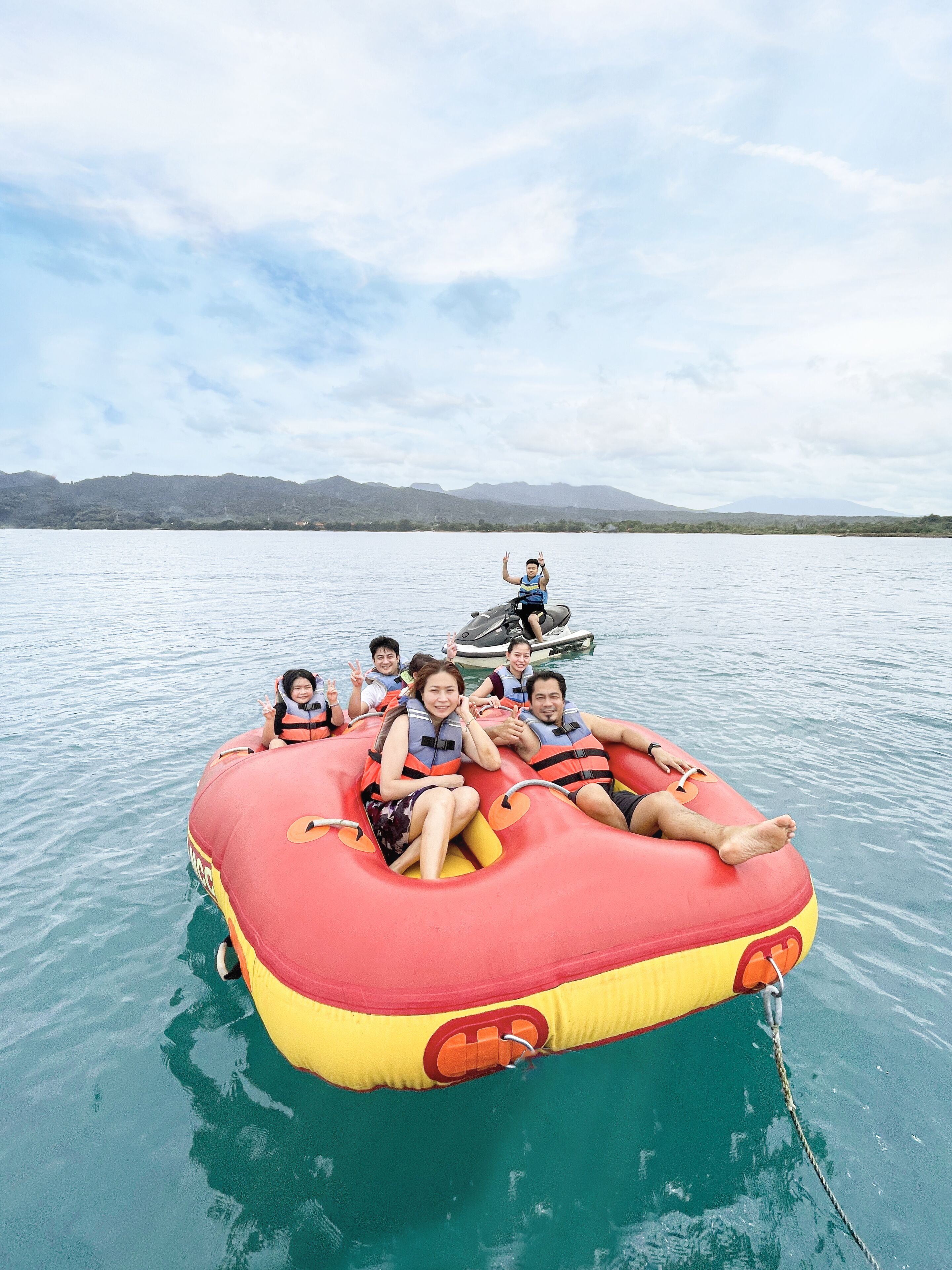 Un groupe de personnes se trouve sur un radeau gonflable rouge et jaune, sur une étendue d’eau calme, avec des montagnes en arrière-plan.