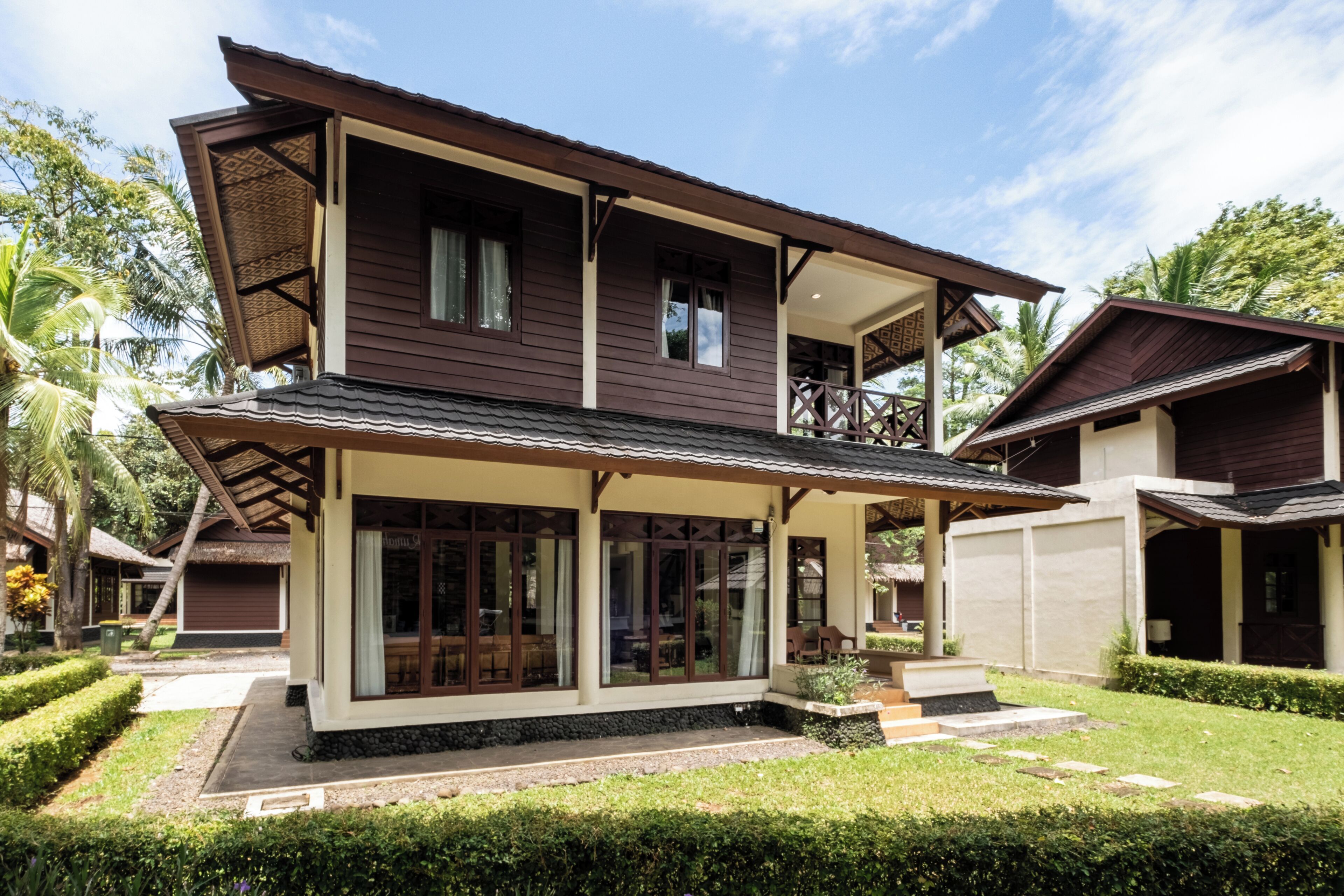 Une maison à deux étages dotée d’un balcon, de grandes fenêtres et d’un jardin bien entretenu.