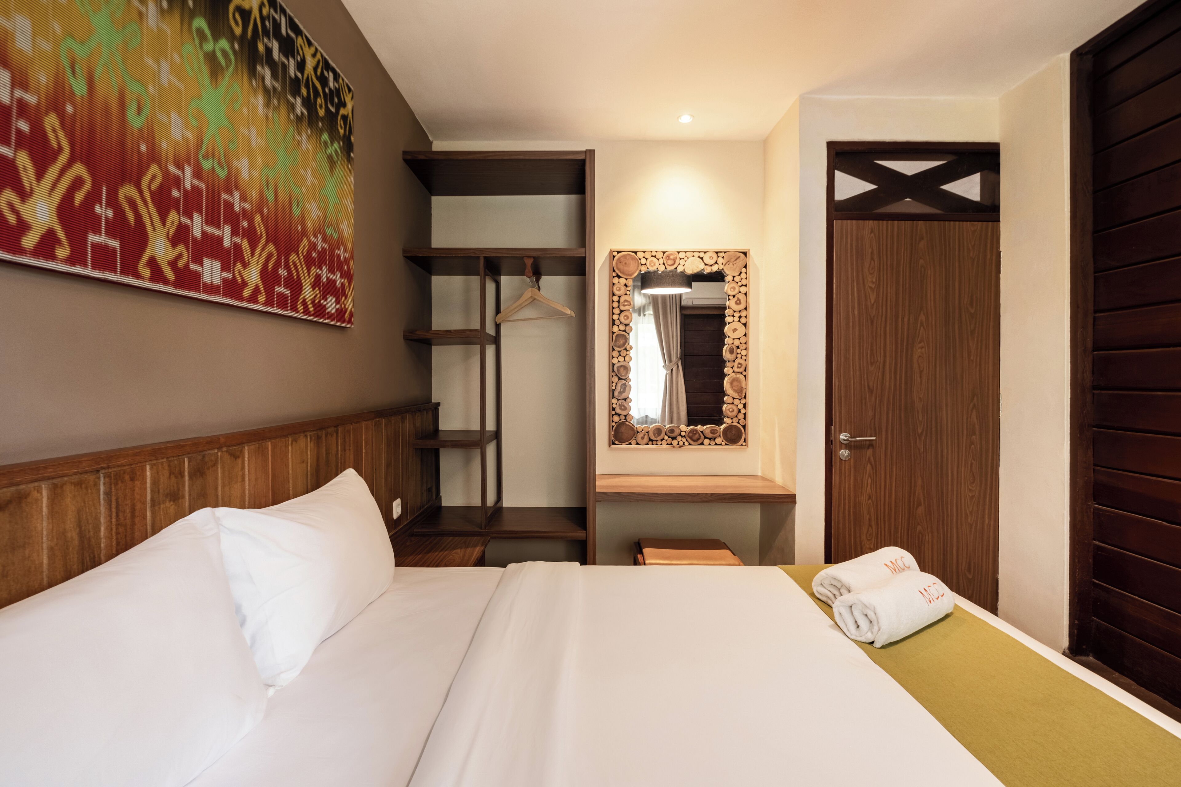 A hotel room with a bed, a wardrobe, a mirror, and a wall art piece.