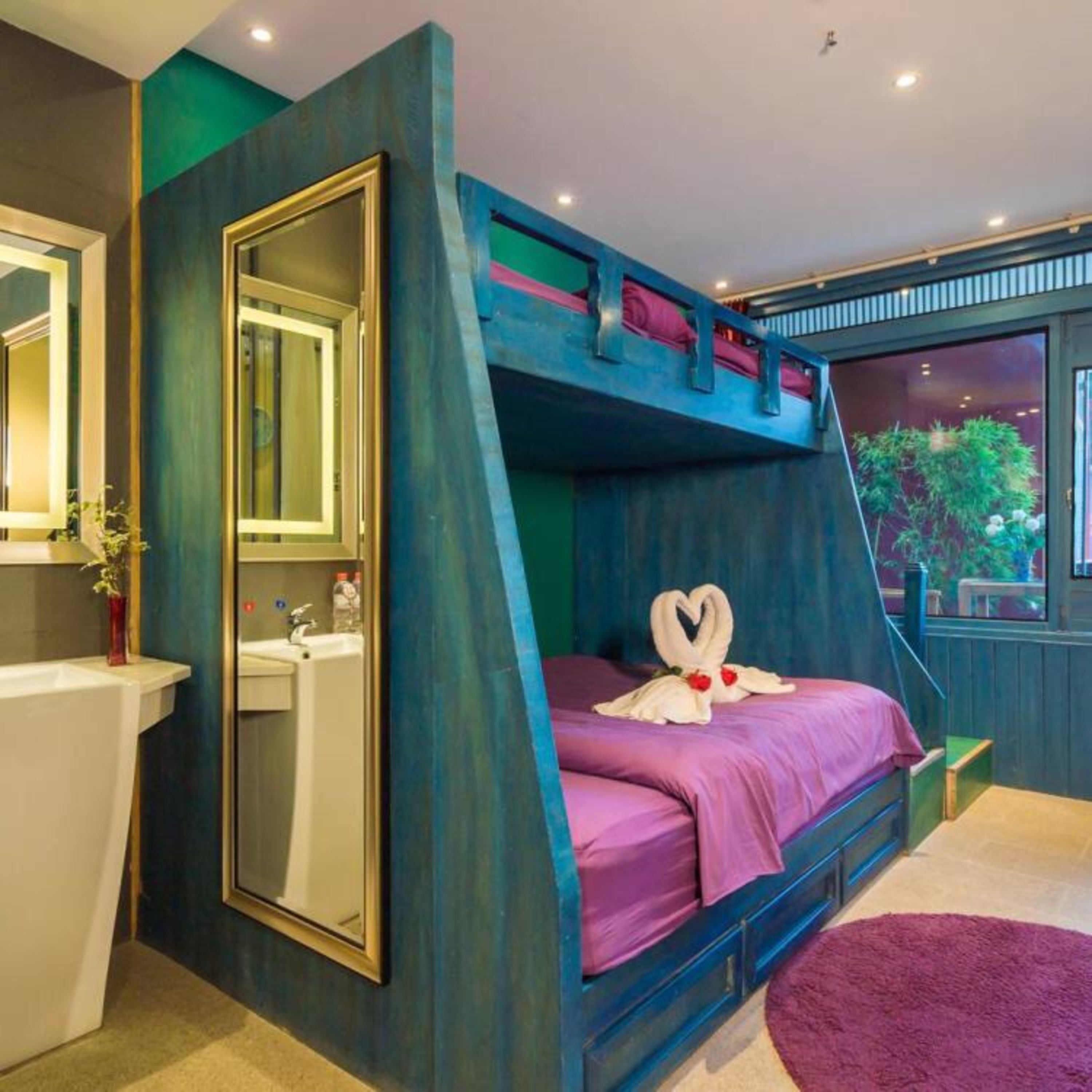 A bunk bed room with a mirror, a sink, and a window with a view of greenery.