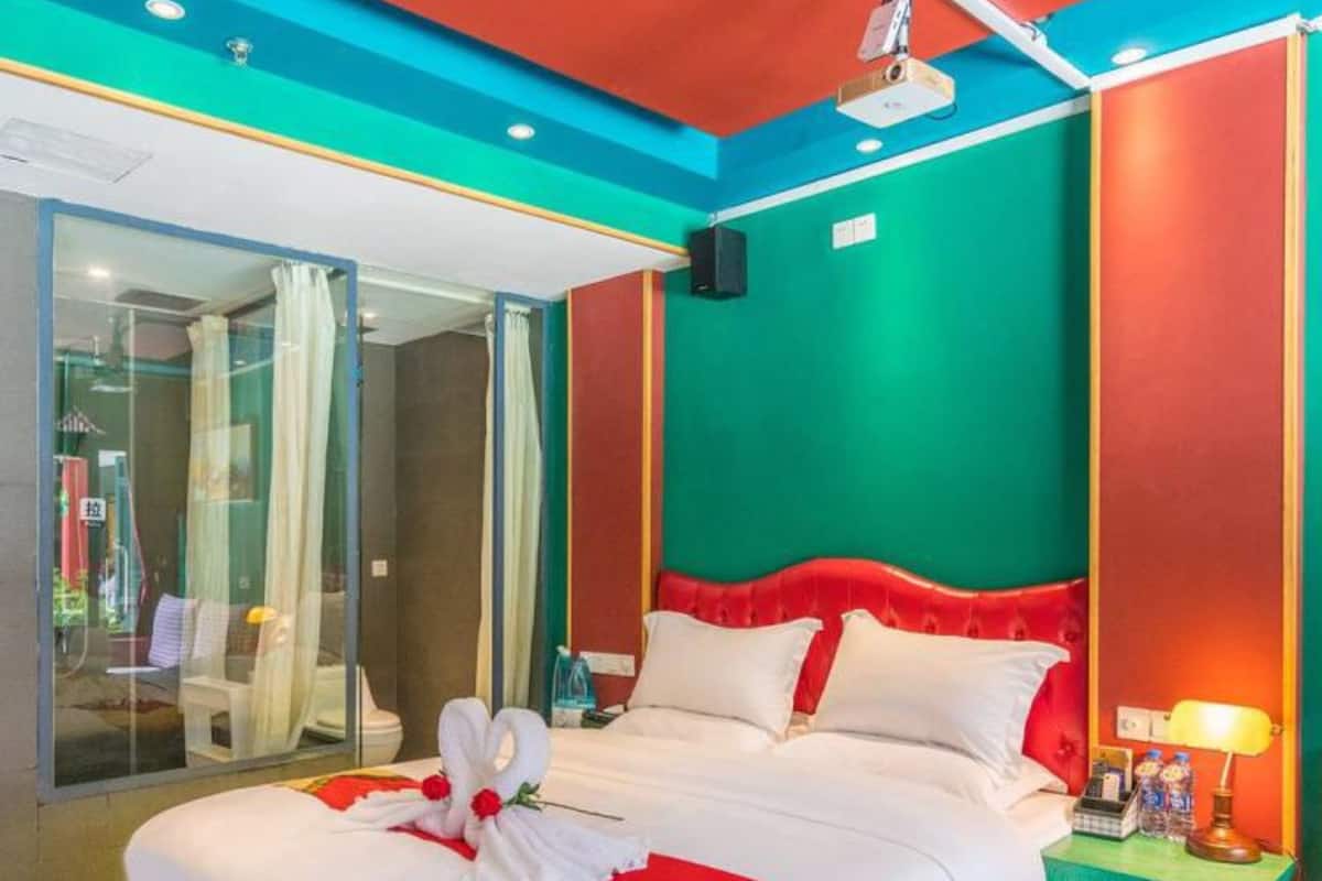 A hotel room with a large bed, a glass shower area, and a colorful wall design.