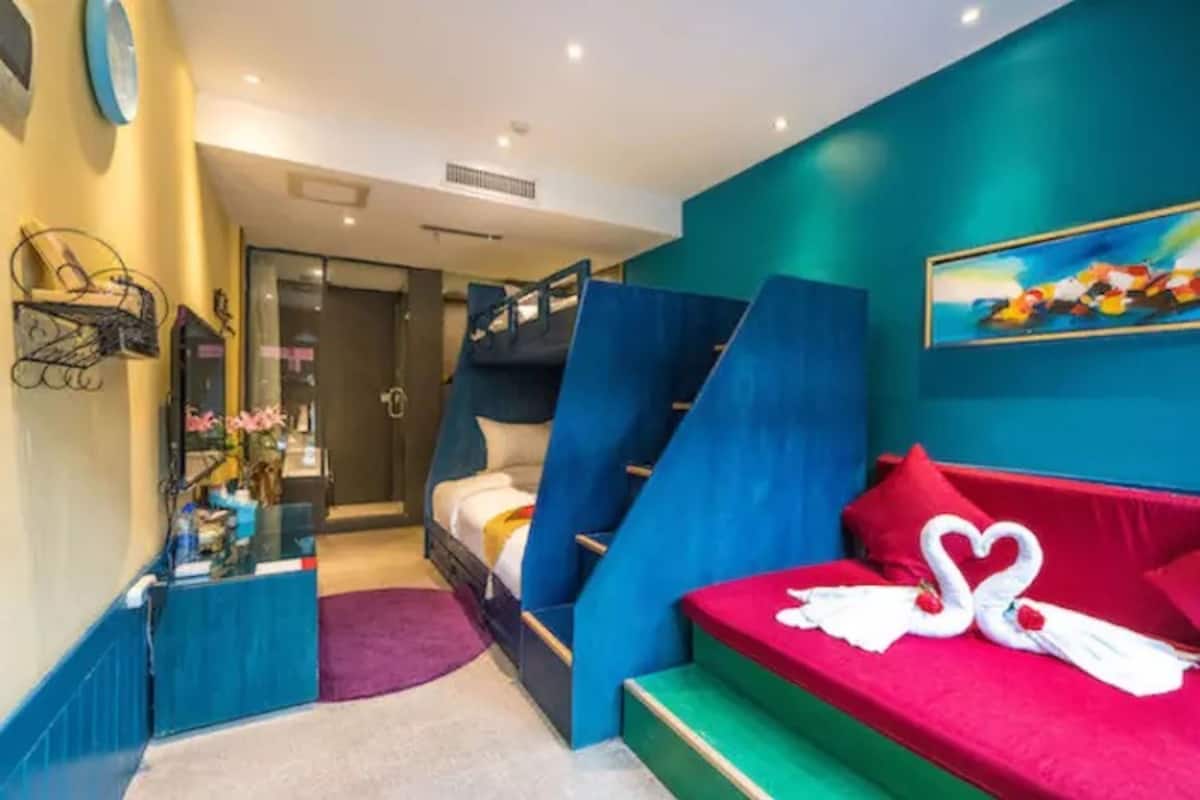 A room with a bunk bed, a desk with a chair, a red sofa, and a painting on the wall.