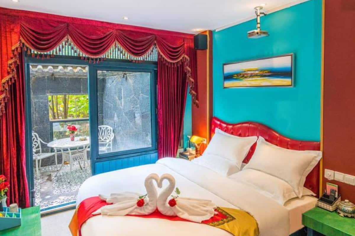 A hotel room with a bed, a window, a painting, and a view of the outdoors.