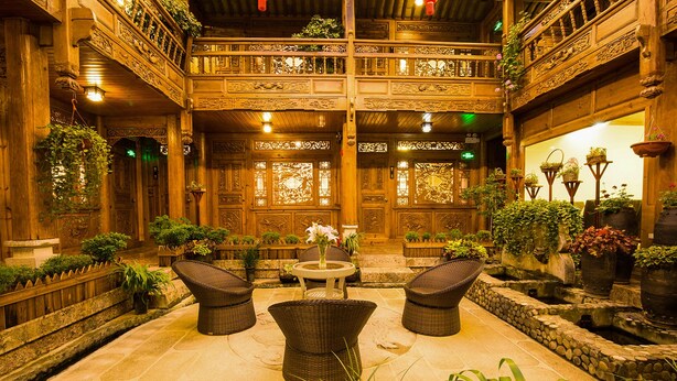 Un intérieur traditionnel en bois, avec un espace salon central, plusieurs niveaux dotés de balcons et diverses plantes en pot.