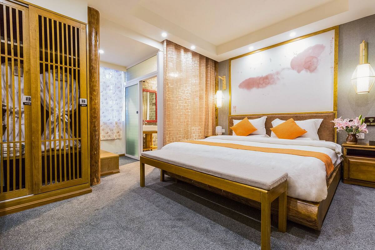 Hotelkamer met een groot bed, een houten garderobe, een badkamer met spiegel en een wand met een groot schilderij.