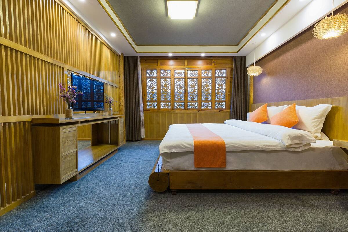 Een hotelkamer met een houten bed, een bureau met televisie en een decoratief raam met ingewikkelde patronen.