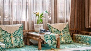 Una habitación tradicional con un sofá de madera, una mesita con tetera y una planta en maceta.