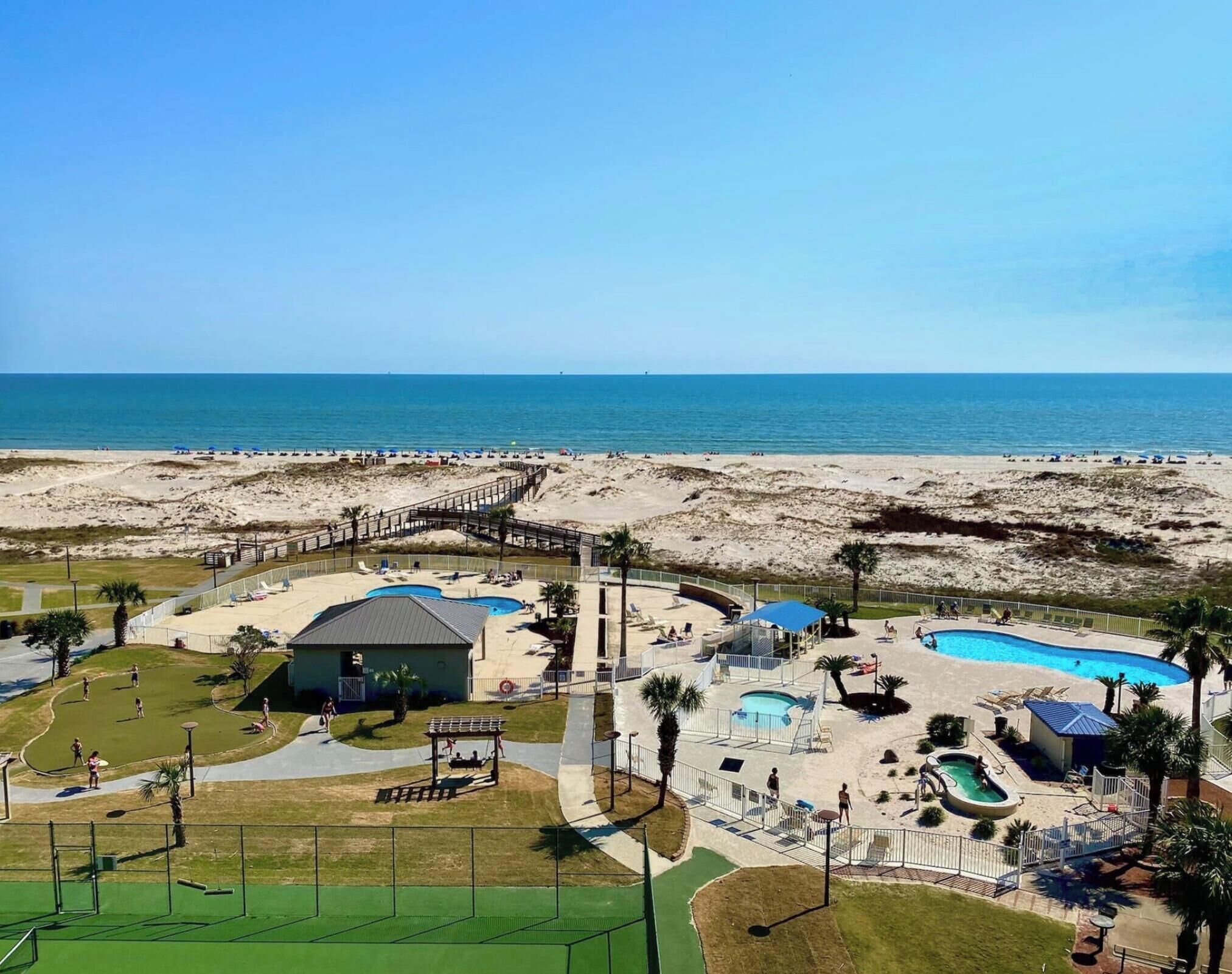 Un complejo turístico en la playa con una piscina grande, un parque infantil y un muelle que da a la playa.