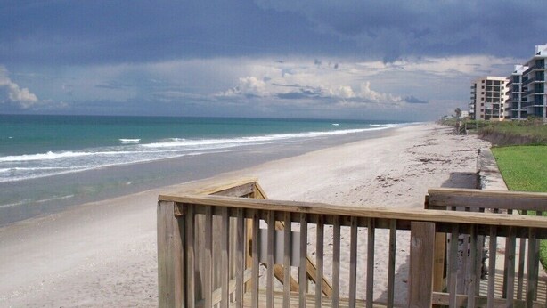 Ein Strand mit einer Holzstege, der zu einem Gebäude führt.