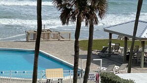 Ein Poolbereich mit Palmen, einem Schild für den Strandzugang und Blick aufs Meer.