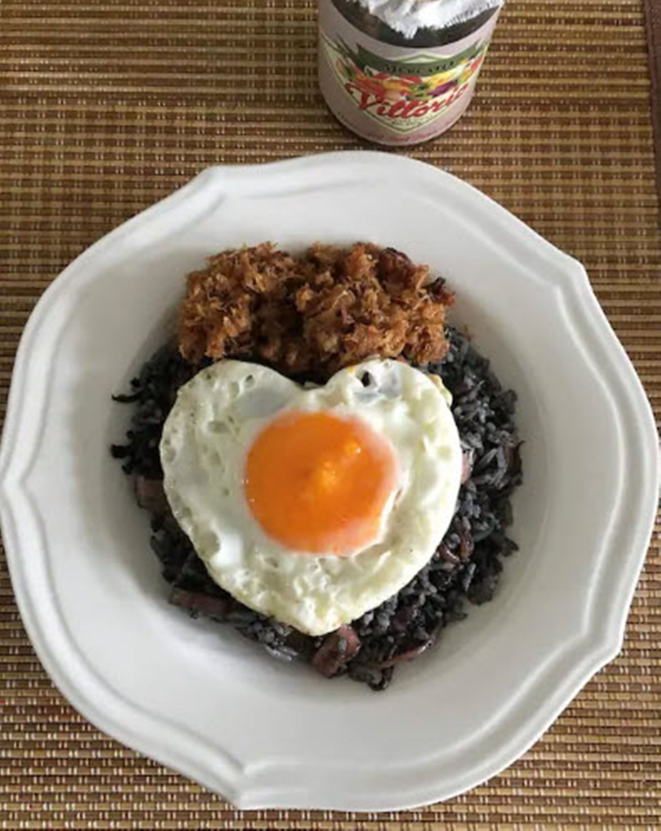 Un plato con un huevo frito sobre arroz negro, acompañado de cebollas fritas.