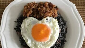 A plate with a fried egg on top of black rice, accompanied by a side of fried onions.